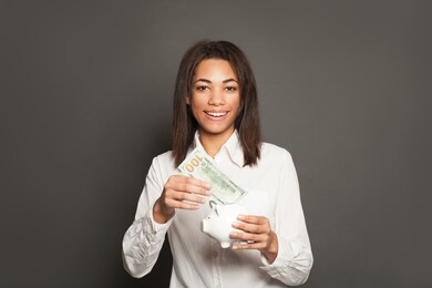 smart successful african american woman putting in piggy bank one hundred dollars banknote