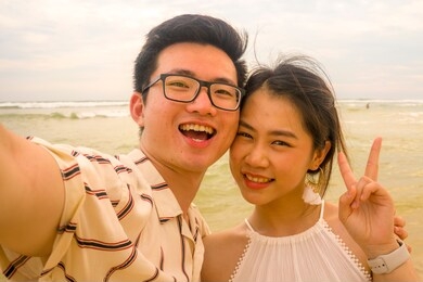 young happy and romantic asian korean couple in love enjoying holiday taking selfie photo together on beautiful beach having fun by the sea playful and affectionate in relationship concept