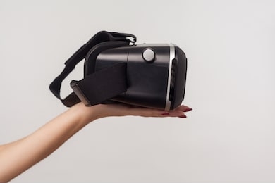 side view of female hand holding vr goggles, virtual reality 3d glasses headset for cyberspace simulation, innovative technologies, future and science. indoor studio shot isolated on gray background