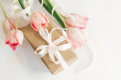 happy mothers day. pink tulips flat lay with ribbon and gift box on white background. stylish soft image of spring flowers. happy womens day. greeting card mockup.  hello spring