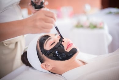 spa and beauty room, black face mask of mud and algae, an asian woman lying on the bed, waiting for a mask expert on a beautiful face.