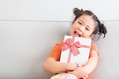 little asian girl smile and excited and holding red gift box on sofa 
 in living room background.child holding gift box in christmas and new year concept.
