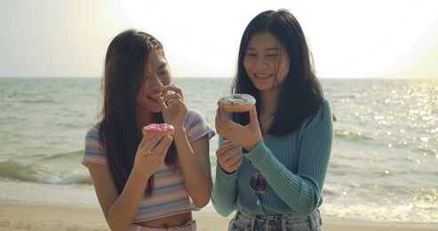 women friends enjoying life eating donuts sweet delicious relaxing and freedom  at beach , attractive together of asian female traveler people lifestyle. 