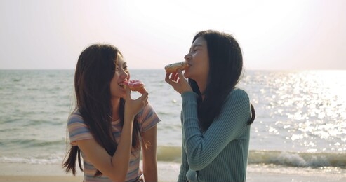 women friends enjoying life eating donuts sweet delicious relaxing and freedom  at beach , attractive together of asian female traveler people lifestyle. 
