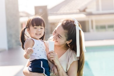 mother holding sun screen cream tube with her daughter near swimming pool.happy mother applying sun cream to little adorable kid girl.sunscreen or sunblock and skincare concept.