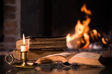 an open bible book with a burning candle in front of fireplace