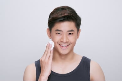 handsome man cleaning face skin with batting cotton pads over white background and looking at camera