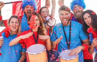 football supporter fans cheering with confetti watching soccer match event at stadium - young people group with having excited fun on sport championship concept - main focus on left man face