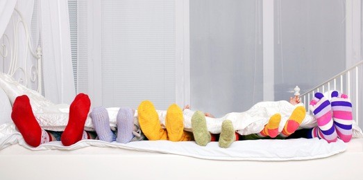 happy family concept. feet of father, mother and four children in colorful knitted socks on white bed. family sleeping together.