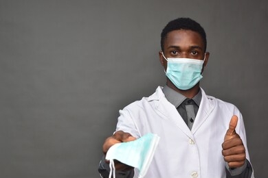 young black man in medical field, wearing a white coat and face mask, offering a face mask
