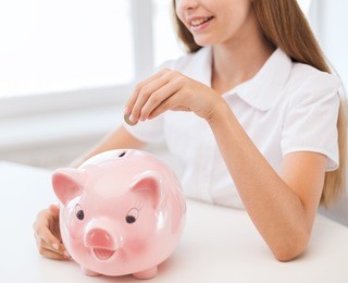education, school and money saving concept - smiling child putting coin into big piggy bank