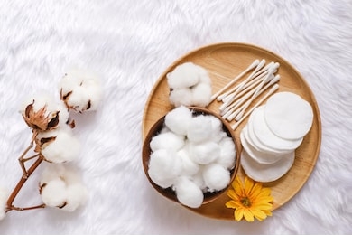 organic cotton facial pads, cotton balls and cotton buds for removal makeup on wooden tray with natural cotton flowers on white fur background, hygiene and healthy care lifestyle  