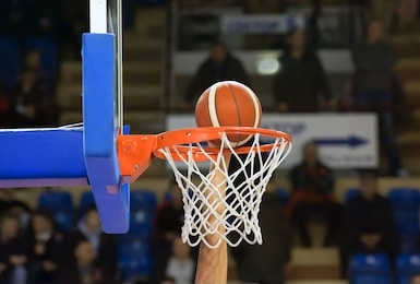 a basketball player throws the ball into the basket with one hand. fans sit on the stands in the background