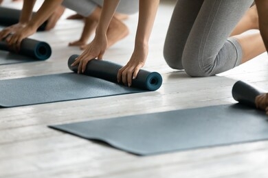 sporty women barefoot kneeling on warm floor fold up personal mats finished yoga session at studio close up. training class like-minded females, healthy body and mind, lifestyle and wellness concept