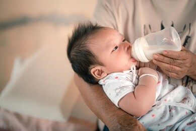 baby is drinking milk from a bottle hold by the mother.