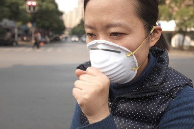 asian woman wearing a protective face mask on a city street with air pollution