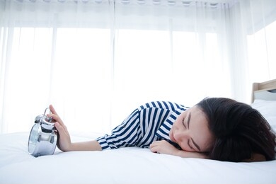 the girl sleeps in bed in the bedroom, the desk clock alarm loudly in the morning she uses her hand to turn off the beep. the concept of resting on the weekends. copy space