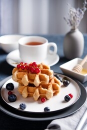 fresh belgian waffles with blueberries and red currants, honey and tea on a dark table. delicious breakfast