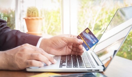 business man hand hold credit card to shopping internet online bill on computer, debit saving purchase buy on table background. shopaholic people retail pay sale money, bank terminal account concept