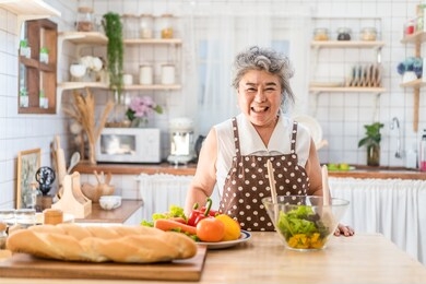 senior asian elder woman happy living in home kitchen. grandmother cooking salad dish standing at counter with happiness and smile enjoy retirement life. older people activity in family at home.
