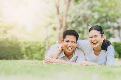 happy asian smiling couple in love relaxing on green grass. couple lying on grass outdoor