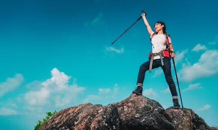 young asian women hikers climbing up on the peak of mountain near ocean. woman hiking in the mountains standing on a rocky summit ridge with backpack and pole looking out over ocean landscape