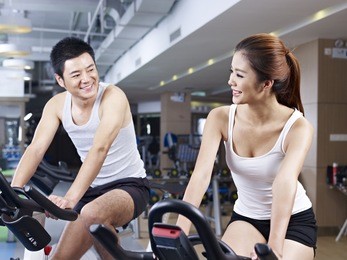 young man and woman talking while exercising on bicycle in fitness center.