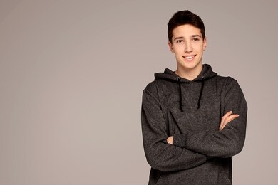 portrait of a handsome teenage boy in hoodie posing over gray background. studio shot. teen fashion.
