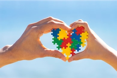 child and adult hands holding colorful heart on blue sky background. world autism awareness day concept