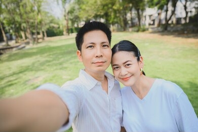 closeup shot of happy smiling asian couple take selfie outdoor. a man taking a photo with his wife in the park