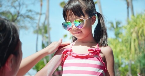 mother applying protective sunscreen lotion on daughter arm nearby swimming pool