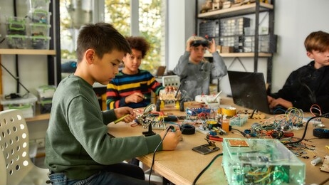 young technicians building robots and vehicles, using soldering iron to join chips and wires, programming toys at stem robotics class. inventions and creativity for kids