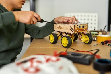cropped shot of a boy using screwdriver while fixing bolts on a robot vehicle. smart kids and stem education. robotics and software engineering for elementary students. selective focus