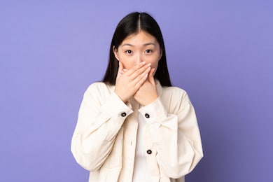 young asian woman isolated on purple background covering mouth with hands