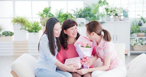 two daughters give flowers to her mom and celebrate happy mother day at home