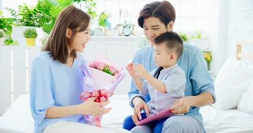 family celebrate happy mother day - father and son give flowers to mom at home