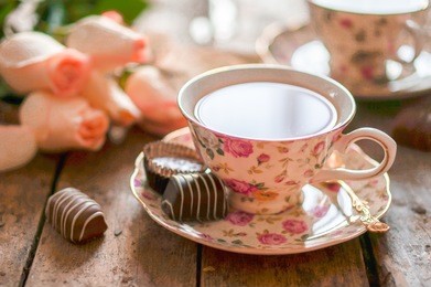 close up of a cup of tea with roses and chocolate candies on wooden table