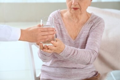 female doctor giving senior woman suffering from parkinson syndrome glass of water in clinic