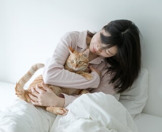 asian woman hugging a cat on the bed