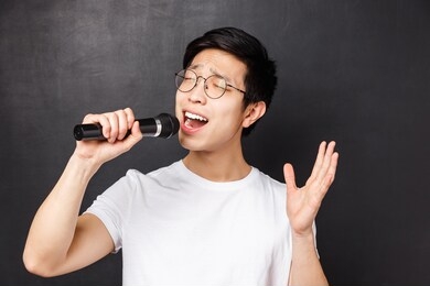 leisure, people and music concept. close-up portrait of passionate and carefree asian guy likes singing songs, holding microphone and raising one hand, perform in fron of friends on karaoke party