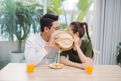 cute couple hiding faces behind the hat in cafe 