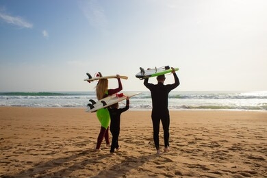 family with surfboards walking on beach. back view of parents with cute little son in wetsuits holding surfboards and walking to ocean waves. surfing concept