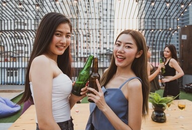two young asian women friends have happiness moment to celebrating dance party with bottle of beer in hand in nightclub.focused on two girl in front blurred other in background.