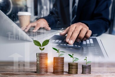 double exposure of business hand doing finances and calculate with tree piles of coins with small trees.