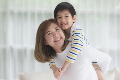 asian child on a piggy back ride with his mother at home