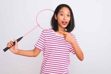 young beautiful chinese woman holding badminton racket over isolated white background very happy pointing with hand and finger