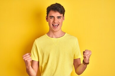 teenager boy wearing yellow t-shirt over isolated background celebrating surprised and amazed for success with arms raised and open eyes. winner concept.