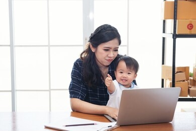 asian business woman working on computer while her daughter. pretty young single mom working at home on a laptop while holding her baby girl. lifestyle business and finance online freelance concept