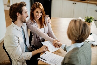 young happy couple shaking hands with insurance agent while having a meeting at home. focus is on young woman. 