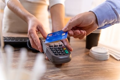 closeup of caucasian man's right hand, holding blue credit card on a pin pad held by a woman's hands